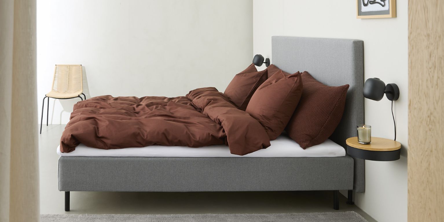 Boxmadrass med rött sänglinne sedd från sidan