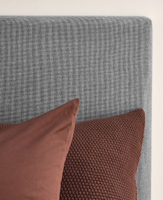 Närbild av grå sänggavel med röda kuddar