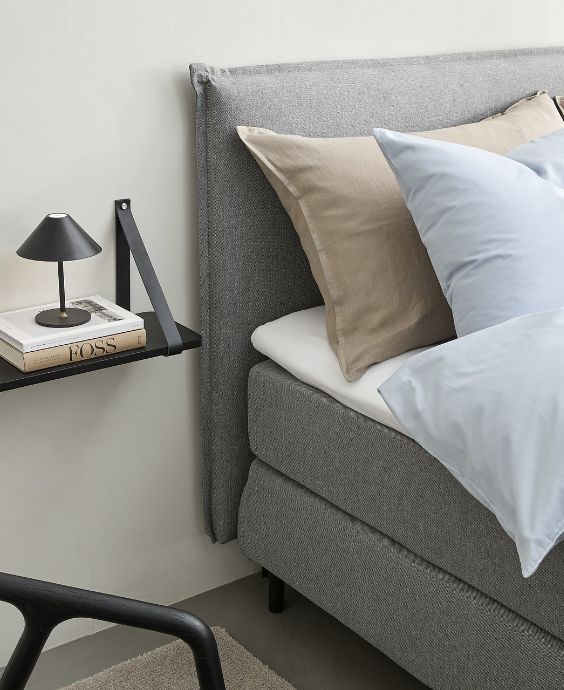 Detalj av kontinentalsäng i grått stående bredvid en vägghylla