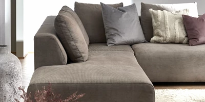 Design uden navn - 2024-12-27T230353.772.jpg Soffa med puffavslutning i grått tyg. I soffan finns en massa kuddar i olika färger