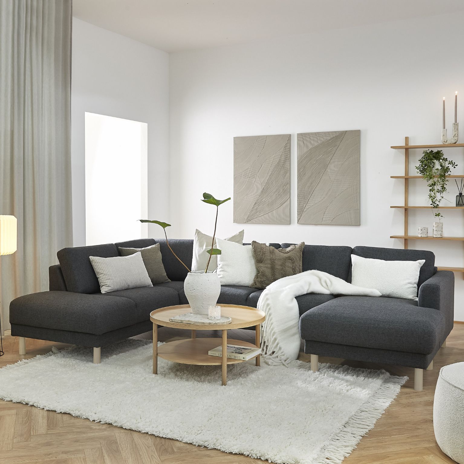 Mysig vardagsrumsmiljö med en U-soffa i centrum. Den står på en vit matta, och det finns också vita kuddar i soffan.