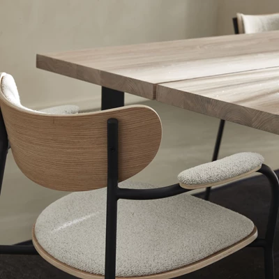 Matsalsstol med böjt ryggstöd och stoppat armstöd och säte. Stolen står vid ett plankbord i trä