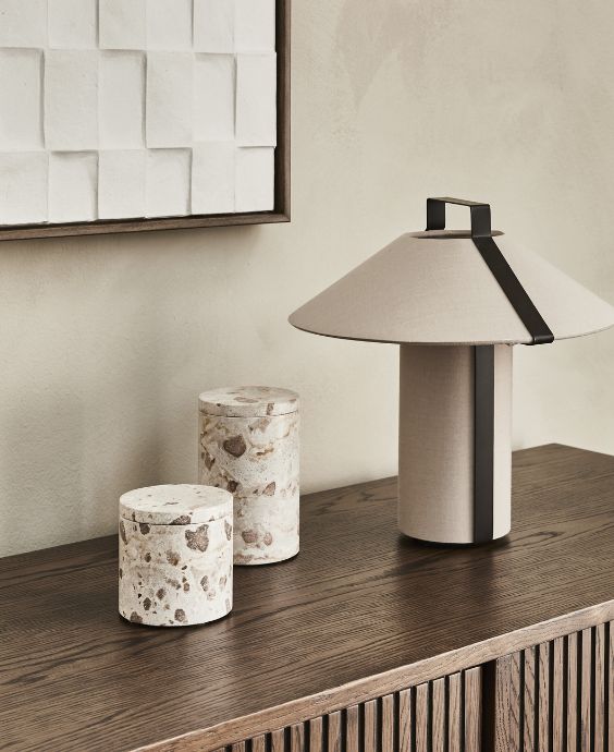 Vit/brun bordlampa stående på en mörkbrun skänk. Bredvid står två krukor med lock.