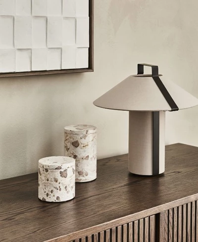 Vit/brun bordlampa stående på en mörkbrun skänk. Bredvid står två krukor med lock.