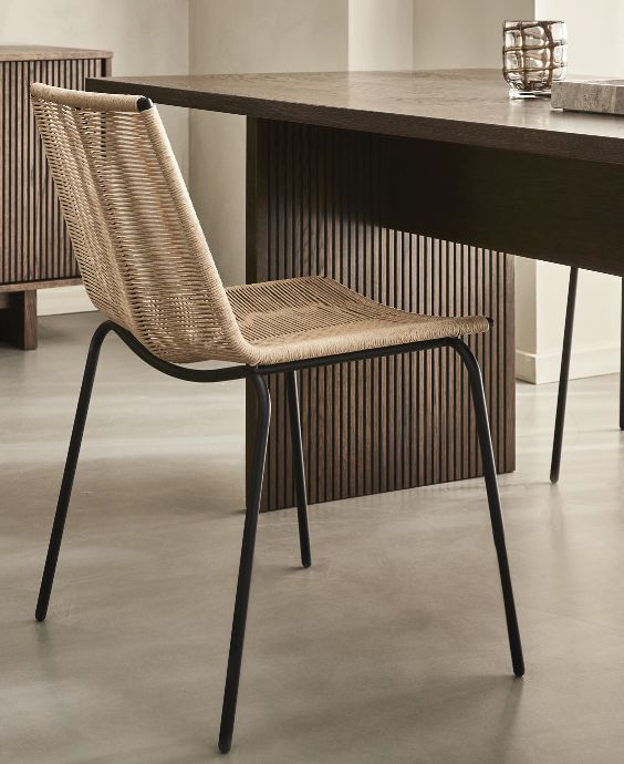 Stol i flätverk med svarta stålben stående vid ett matbord i mörkbrunt trä