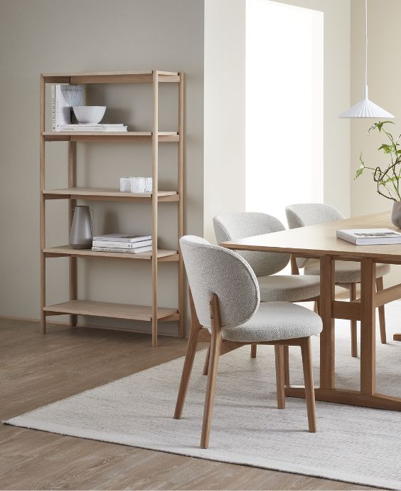 Matsal med träbokhylla, matbord i Shakerstil i trä och stoppade stolar i grått.