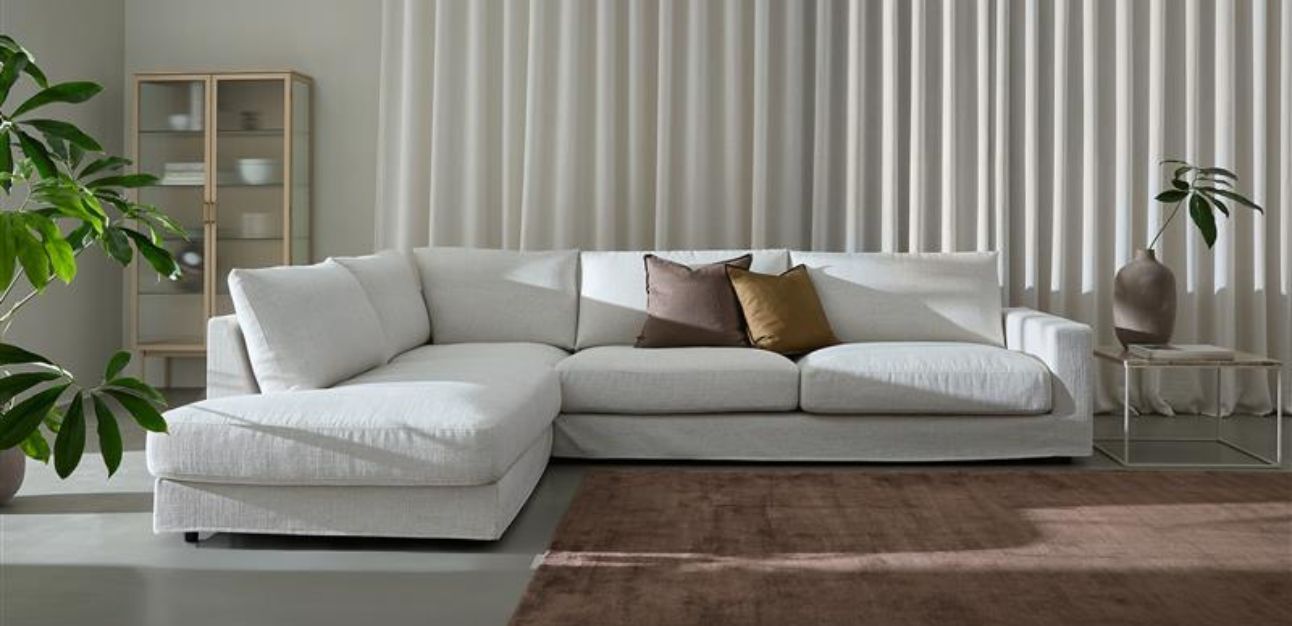 Stor vit hörnsoffa med kuddar och krukväxter