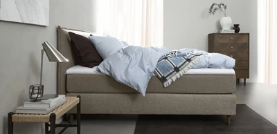 Design uden navn - 2025-01-16T140613.529.jpg Kontinentalsäng i ljusgrå färg stående i ett sovrum i nordisk stil.