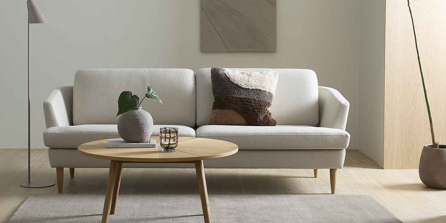 Klassisk och stilren soffa i vita nyanser stående bredvid en golvlampa. Framför står ett runt soffbord