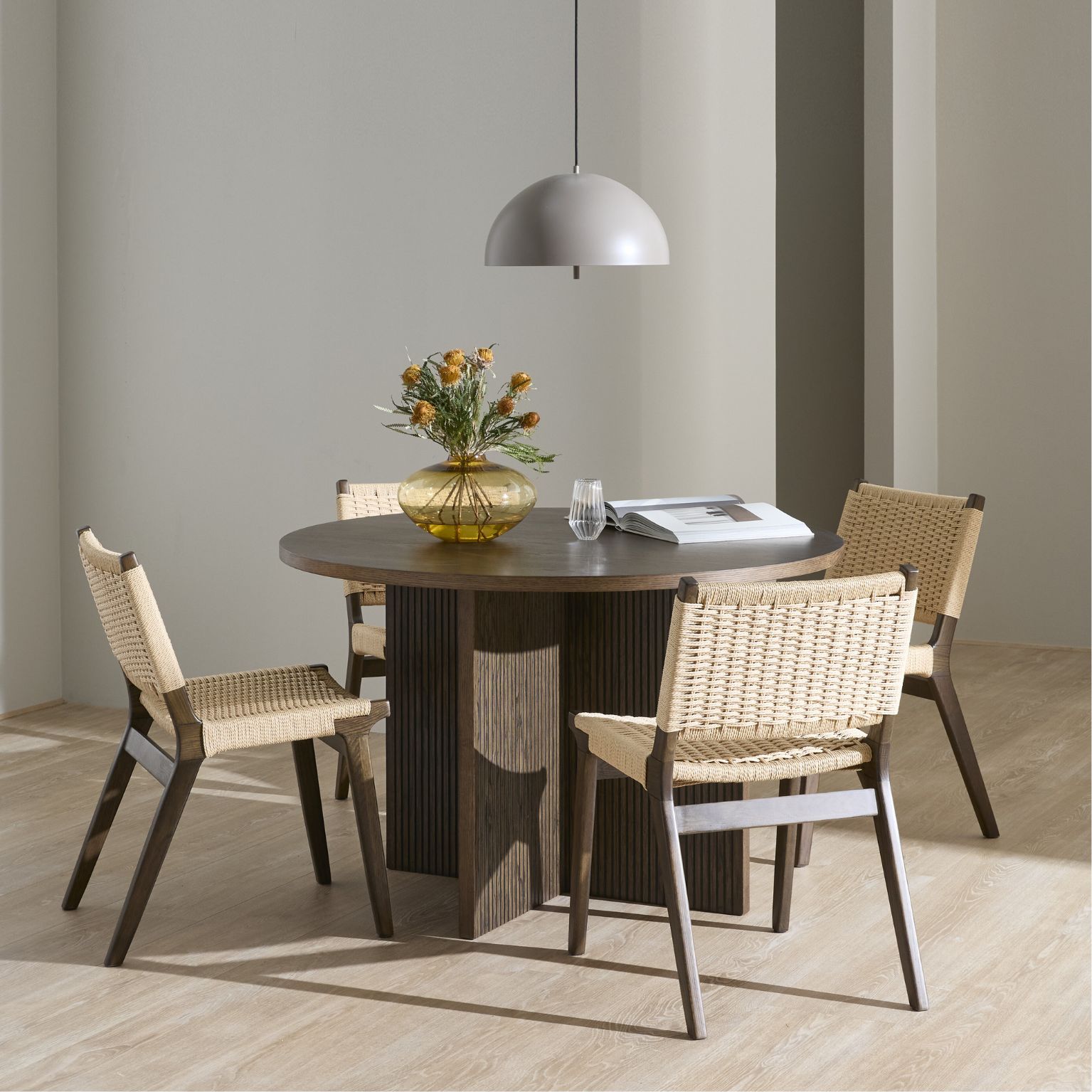 Runt matbord i mörkt trä tillsammans med fyra matstolar i samma träslag, men med sits och rygg i flätad design.