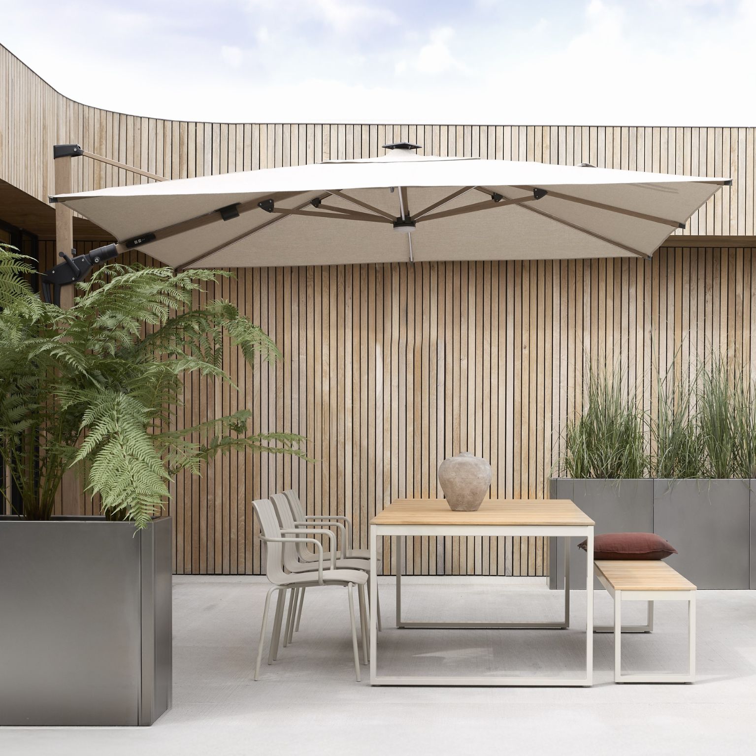 Utomhusmiljö med trädgårdsbord, bänk, trädgårdsstolar och ett stort parasoll med solcell