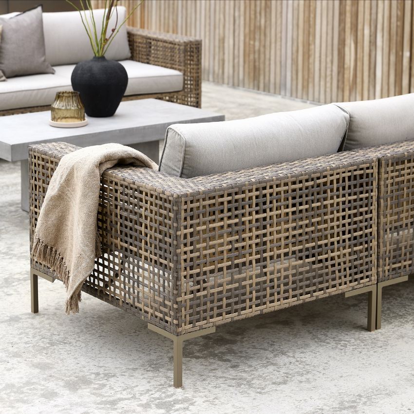 En loungesoffa i flätat material sedd bakifrån. Soffan har grå dynor.