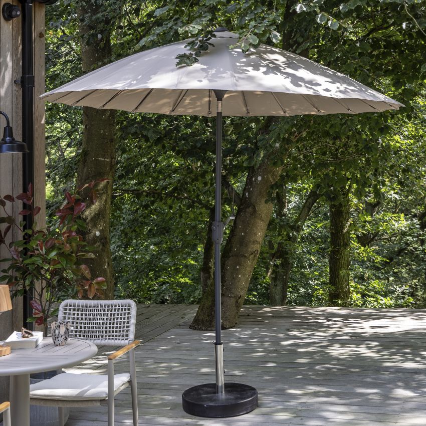 Parasol med grå duk och svart stomme stående framför gröna träd.