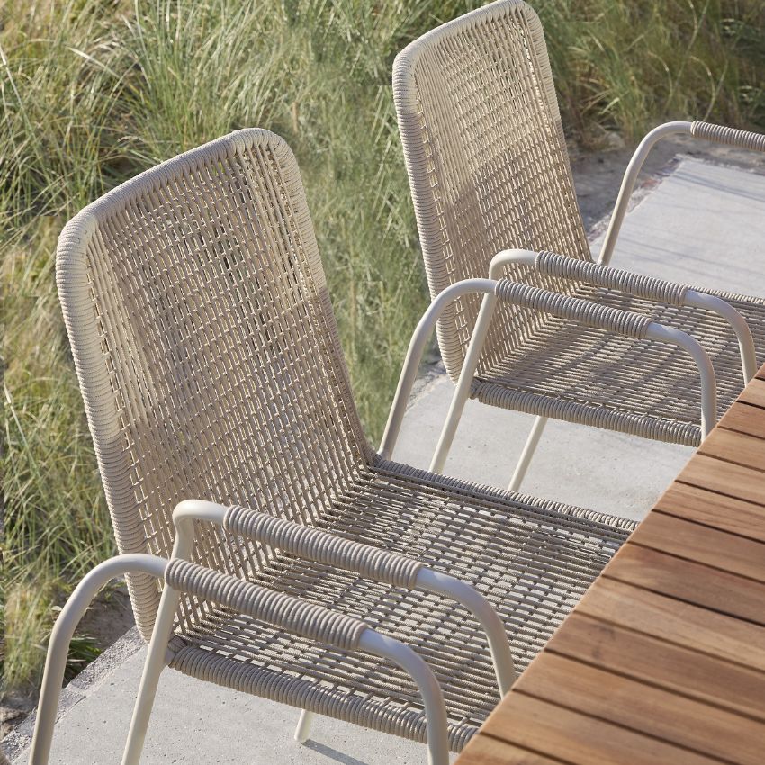 Två trädgårdsstolar i grå aluminium och grå flätning stående vid ett trädgårdsbord i trä.