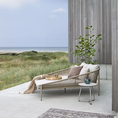 Modern solstol på en terrass med havsutsikt, omgiven av växter och en utomhusmatta.