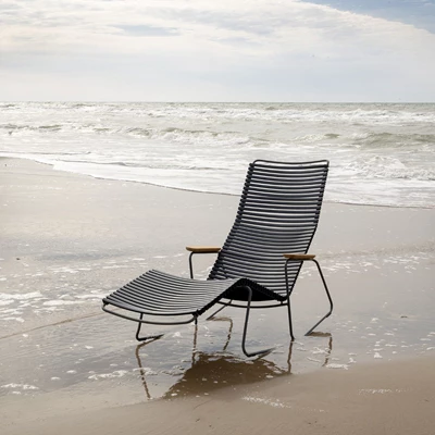 Modern svart solstol på stranden, delvis i vattnet, mot havet.