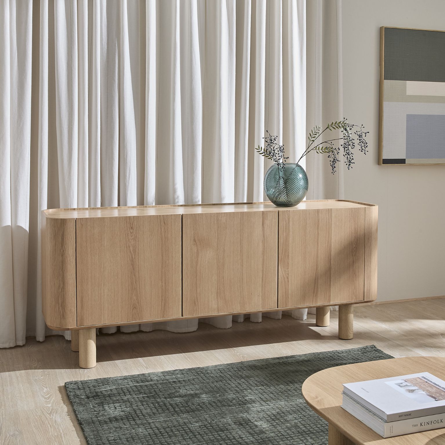 Skänk i trä med tre dörrar framför sandfärgade gardiner