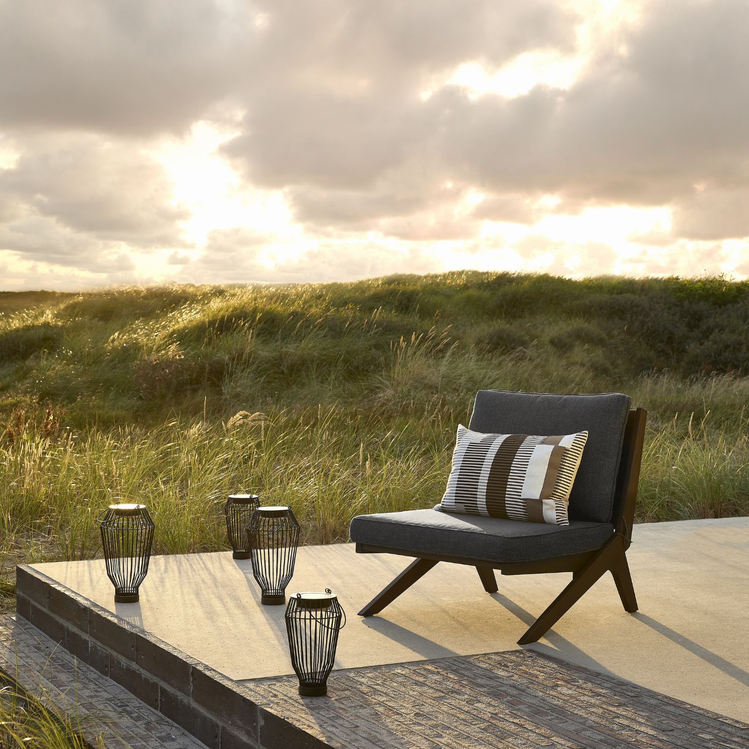 Loungefåtölj med svarta solcellslampor framför. Bakom är solen på väg ner vid horisonten.