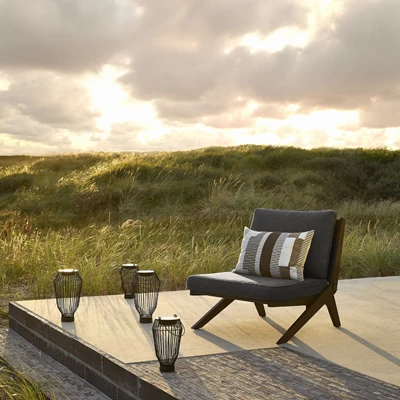 Loungefåtölj med svarta solcellslampor framför. Bakom är solen på väg ner vid horisonten.
