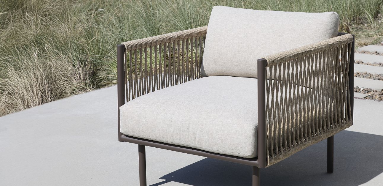 Loungefåtölj med grå dynor och flätad sits och rygg