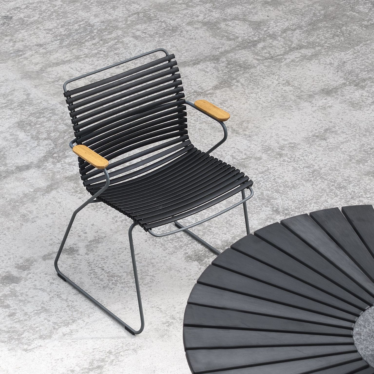 Trädgårdsstol med svarta lameller och armstöd i bambu vid ett svart, runt bord