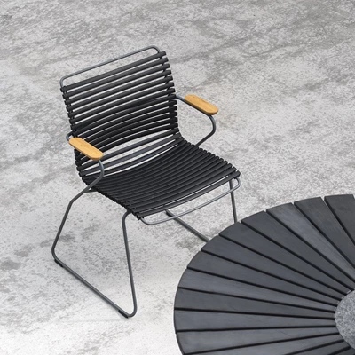 Trädgårdsstol med svarta lameller och armstöd i bambu vid ett svart, runt bord