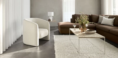 Vit helklädd Loom loungestol i en varm, inbjudande vardagsrumsinredning med en brun soffa, en crèmefärgad matta och ett minimalistiskt marmorbord.