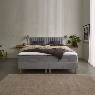 Ett modernt sovrum med en grå ställbar säng, stoppad sänggavel med vertikala paneler och eleganta träben