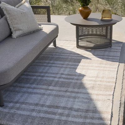 Mysigt utomhus hörn med stil: En inbjudande terrass med en ljus matta, bekväma soffkuddar och ett modernt lågt bord, idealiskt för en avkopplande eftermiddag utomhus.