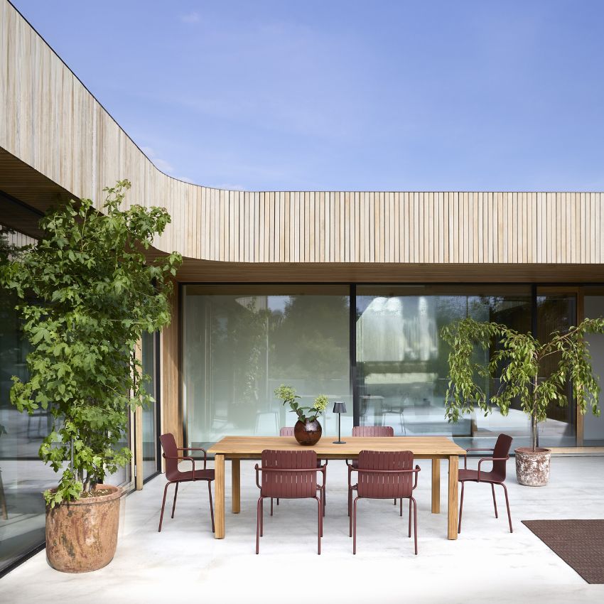 Modern uteplats med trädgårdsmöbler, växter och välvd träfasad.