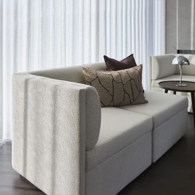 Närbild av beige soffarm med mjukt, texturerat tyg, belyst av naturligt ljus.