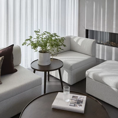 Inblick i ett vardagsrum med en vit soffa uppdelad i flera moduler. Mellan soffmodulerna finns bland annat ett brunt sidobord och i mitten ett brunt soffbord.