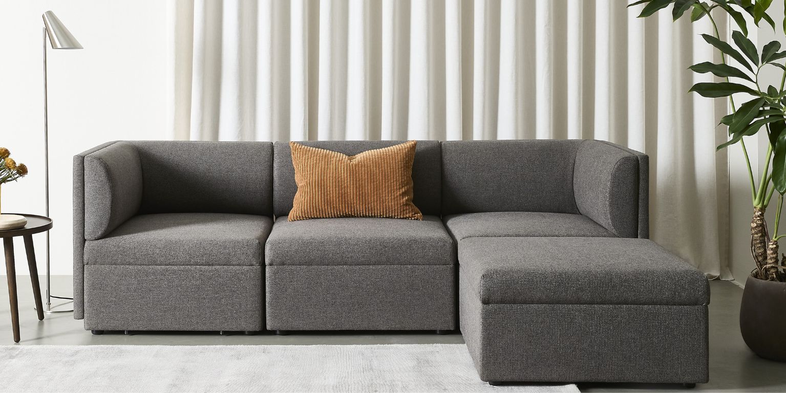 Modern, gråaktig soffa med rundade armstöd och ryggkuddar.