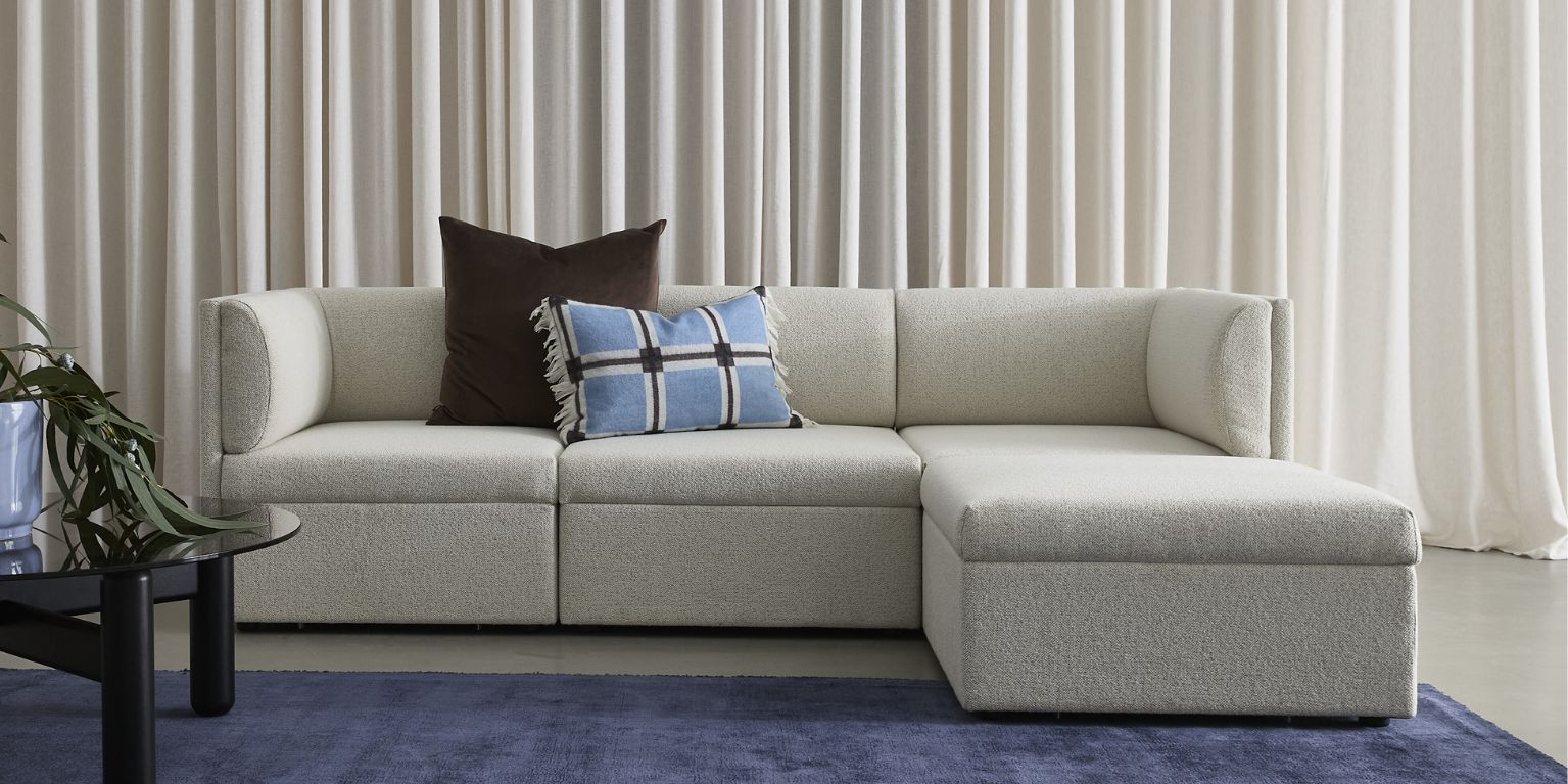 Modern, vitaktig soffa med rundade armstöd och ryggkuddar.