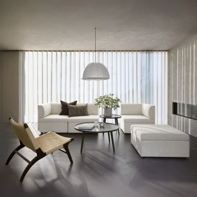 Vardagsrum i vita och grå nyanser. I centrum står en vitaktig soffa uppdelad i flera moduler. I förgrunden syns en fåtölj med flätad sits och ryggstöd.