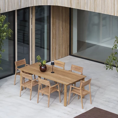 Modernt utomhus matområde med träbord och stolar, uppställt på en plattad terrass med glasfasad