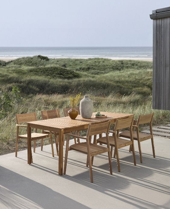 Utomhus matområde med träbord och stolar, uppställt på en terrass med utsikt över en sanddyn