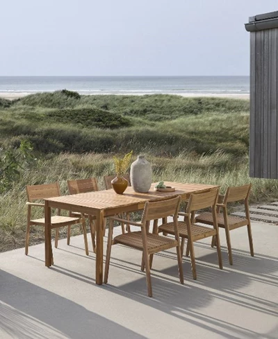 Utomhus matområde med träbord och stolar, uppställt på en terrass med utsikt över en sanddyn