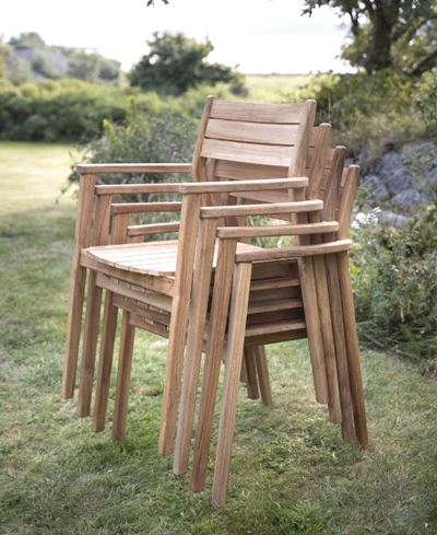 Staplade trästolar i en trädgård med gräs och buskar i bakgrunden