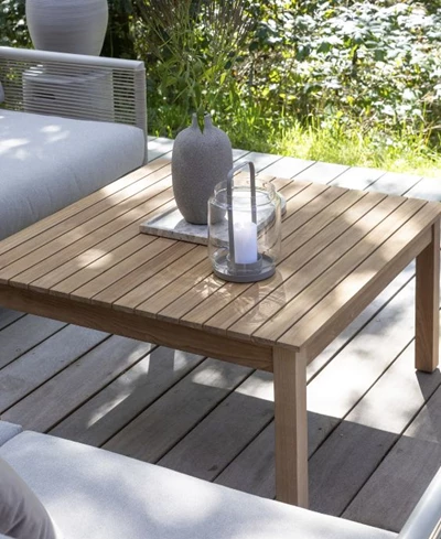 Litet träbord med föremål placerade på, omgivet av vita kuddar och beläget på en träterrass