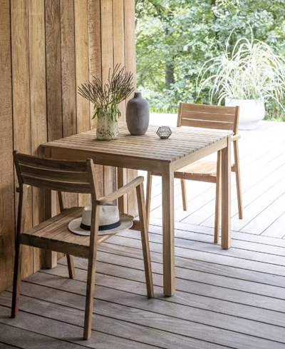 Trädgårdsbord i trä med en vas och stol på en träveranda omgiven av gröna växter