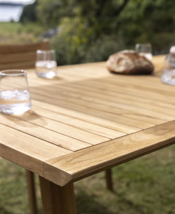 Närbild av ett träbord med dricksglas och en brödkorg, utplacerat utomhus