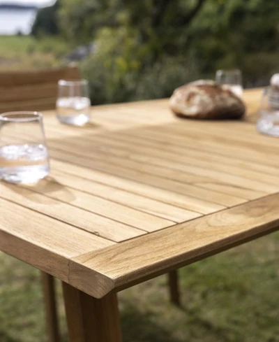 Närbild av ett träbord med dricksglas och en brödkorg, utplacerat utomhus