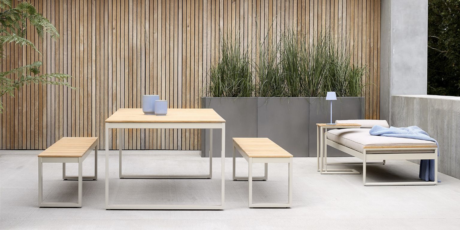 Minimalistiskt utomhus loungeområde med moderna trä- och metallbord och bänkar, placerade på en betongterrass.