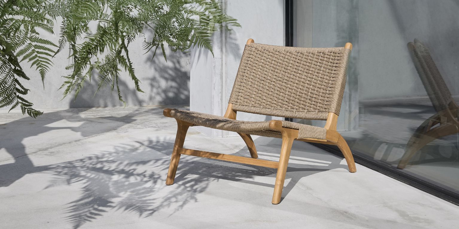 Modern flätad träfåtölj placerad på en betongterrass med palmblad som kastar skuggor