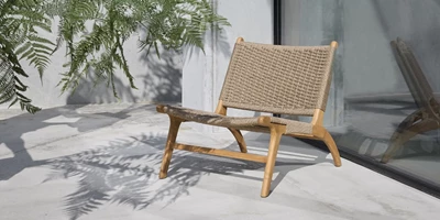 Design uden navn - 2025-02-25T113152.131.jpg Modern flätad träfåtölj placerad på en betongterrass med palmblad som kastar skuggor