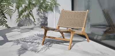 Elegant loungestol med flätad sits och träram placerad på en utomhusterrass med skuggor från växter.
