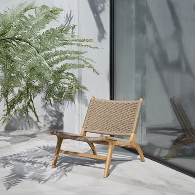 Elegant loungestol med flätad sits och träram placerad på en utomhusterrass med skuggor från växter.