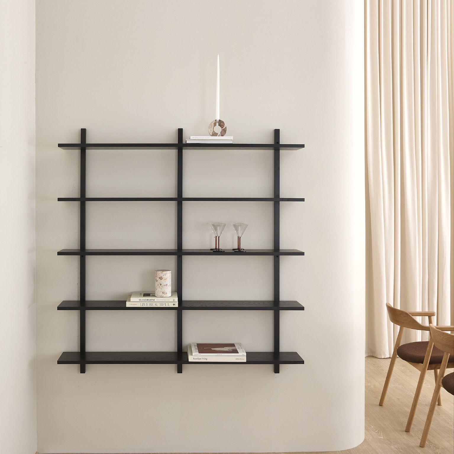 Modern svart vägghylla med flera hyllplan i ett ljust vardagsrum.