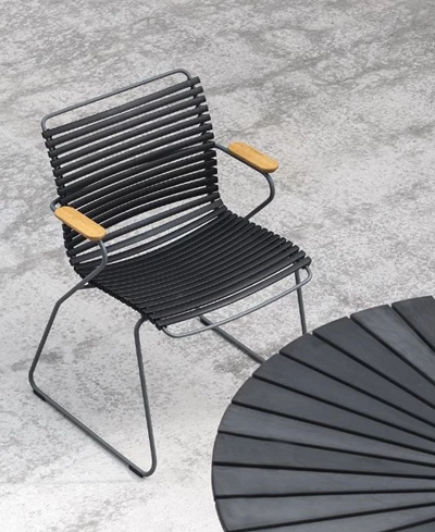 Svart stålramstol med dynor och träarmstöd, placerad på en terrass.